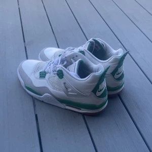 Nike SB Jordan 4 sneakers vit/grön - Nike SB Jordan 4 sneakers i vitt och grönt med meshpaneler, gröna detaljer och klassisk Jumpman-logga på plösen. Skorna har snörning, platt sula och rund tå. Kombination av skinn och syntetmaterial ger en clean och sportig vibe. Perfekt för dig som gillar streetstyle och sneakers med edge.