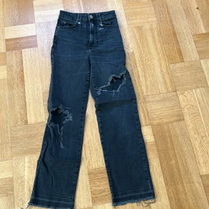 Svarta ripped jeans från Zara, strl 34 - Snygga svarta jeans från Zara med hög midja och raka ben. Jeansen har slitna detaljer och stora hål vid knäna för en edgy look. Fransade benslut och klassisk femficksdesign. Perfekta för dig som gillar streetstyle och vill sticka ut.