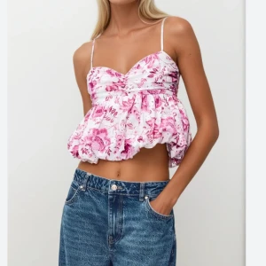 Blommig vit och rosa linnetopp - Superfin croppad linnetopp från Zara med blommigt mönster i rosa och vitt. Toppen har tunna axelband, omlott vid bysten och en puffig, volangig nederdel som ger en söt och trendig look. Perfekt för varma dagar och sommarhäng.