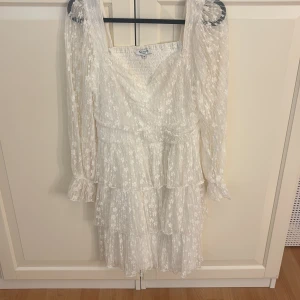 Vit spetsklänning med volanger från bubbleroom  - Superfin vit kortklänning från bubbleroom med transparenta långärmar och flera lager volanger. Klänningen har ett blommigt spetsmönster, v-ringad hals och markerad midja. Perfekt för dig som ska ta studenten! Orginal priset på hemsidan är 999kr. 