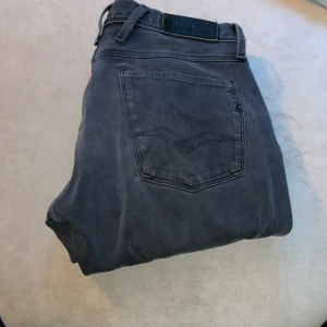 Replay Anbass jeans mörkgrå 31 - Snygga Replay Anbass jeans i mörkgrå färg med klassisk femficksdesign och diskret broderad bakficka. Jeansen har en modern passform och är tillverkade i mjukt jeansmaterial som sitter skönt hela dagen. Perfekt för dig som gillar stilrena och coola jeans.