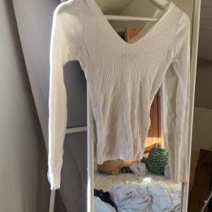 Vit ribbad långärmad topp från mango - Säljer en vit ribbad topp med lång ärm och snygg v-ringning. Den är figurnära och har en stilren look som passar perfekt till jeans eller kjol. Materialet är mjukt och stretchigt, vilket gör den skön att bära hela dagen.