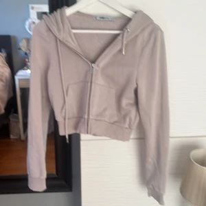 Beige croppad hoodie med dragkedja - Säljer en beige croppad hoodie från new yoker med dragkedja framtill och snörning i huvan. Tröjan har långa ärmar och en stor ficka på magen. Perfekt för chill dagar och enkel att matcha med jeans eller leggings.