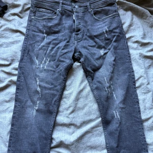 Svarta jeans från Dsquared2, storlek 34 - Säljer ett par svarta jeans från Dsquared2 Jeansen har klassisk femficksdesign, knappgylf och tydliga Dsquared2-detaljer vid linningen och bakfickan. Passformen är rak och materialet är mjukt denim.