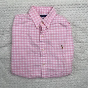 Rosa rutig skjorta från Polo Ralph Lauren - Säljer en klassisk rosa och vit rutig skjorta från Polo Ralph Lauren i storlek M. Skjortan har lång ärm, knappar framtill och broderad logga på bröstet. Perfekt för dig som gillar en tidlös och fräsch stil.
