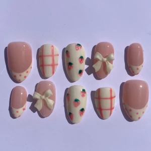 Söta press-on naglar med jordgubbar - Supergulliga press-on naglar i rosa och vitt med jordgubbsmönster, rutigt och små prickar. Några naglar har 3D-rosetter i vitt för extra söt vibe. Perfekt för dig som vill ha en unik och lekfull nagelstil.