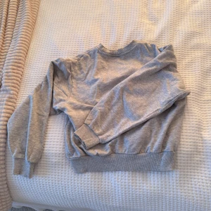 Grå sweatshirt med rund hals - En enkel och stilren grå sweatshirt med rund hals och långa ärmar. Tröjan har ribbade muddar vid ärmslut och nederkant, vilket ger en skön och avslappnad passform. Perfekt att slänga på sig när du vill vara bekväm och ändå se fräsch ut.