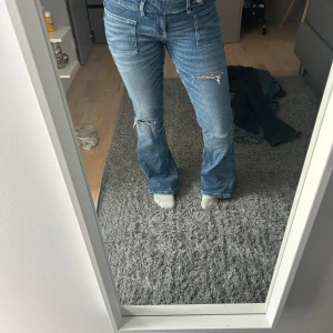 Blå bootcut jeans med slitningar - Säljer ett par blå bootcut jeans med snygga slitningar på låren och knäna. Jeansen har låg midja, raka fickor fram och klassiska bakfickor. Materialet är jeans och passformen är loose med utsvängda ben. Jeansen är helt slutsålda på hemsidan. Aldrig använda