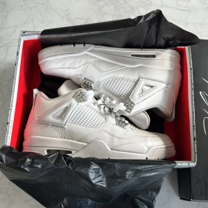 Nike Air Jordan 4 Pure Money sneakers - Nike Air Jordan 4 Pure Money sneakers i helvitt skinn med silverdetaljer och meshpaneler. Klassisk siluett med snörning, platt sula och Jumpman-logga på plösen och hälen. Snygga detaljer i metall och broderad text 'PURE$' på insidan av plösen. Perfekt för dig som gillar clean och stilren look.