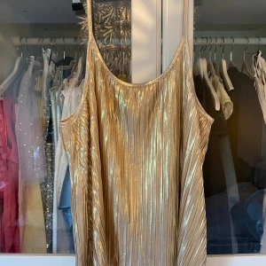 Glittrig guldplisserad linne/ kortklänning - Säljer en glittrig kortklänning i guld med plisserat tyg och tunna axelband. Klänningen har en loose passform och skimrar snyggt!