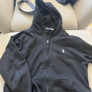 Svart hoodie från Polo Ralph Lauren - Svart hoodie från Polo Ralph Lauren med klassisk vit logga, det finns inga snören till hoodien 