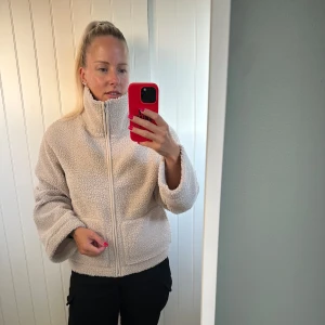 Beige teddyjacka med dragkedja - Mysig beige teddyjacka med hög krage och hel dragkedja framtill. Jackan har två fickor och en loose passform som ger en chill vibe. Perfekt för kalla dagar när du vill vara både bekväm och snygg. Använd 1 gång 