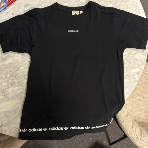 Svart Adidas t-shirt med logga - Svart t-shirt från Adidas med klassisk vit logga broderad på bröstet och tryckt Adidas-tryck. Rund hals och korta ärmar. Skön passform 