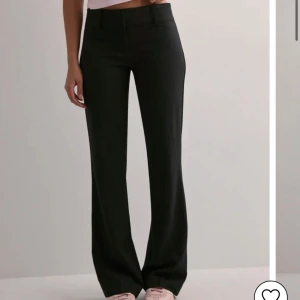 Svarta kostymbyxor med wide fit - Snygga svarta kostymbyxor med låg midja och wide fit. Byxorna har klassisk rak design, bälteshällor och diskret knappstängning fram. Perfekta för en clean och stilren look, matcha med sneakers eller boots för att höja outfiten. Endast testade då de är för stora på mig.