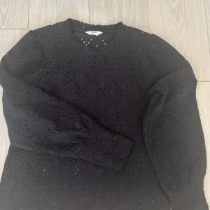 Svart spetsblus från Vero Moda  XS - Säljer en svart blus från Vero Moda i  storlek XS. Blusen har ett snyggt spetsmönster med håldetaljer och långa ärmar med lätt puff vid axlarna. Perfekt för dig som gillar detaljer och vill ha en unik topp i garderoben.