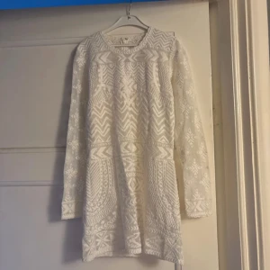 Vit spetsblus/kortklänning Isabel Marant x H&M - Superfin vit kortklänning från Isabel Marant pour H&M med spets och broderade detaljer. Klänningen har lång ärm, v-ringning och ett unikt mönster i spets. Materialet är en mix av bomull och polyester, perfekt för sommarens alla tillfällen.