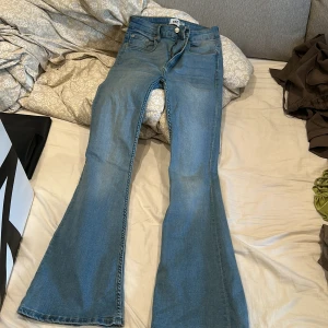 Blå bootcut jeans med utsvängda ben - Snygga ljusblå jeans med bootcut-modell och klassisk femficksdesign. Jeansen har utsvängda ben och normal passform i midjan. Perfekta för dig som gillar retrovibbar och vill ha ett par jeans som sticker ut lite extra.