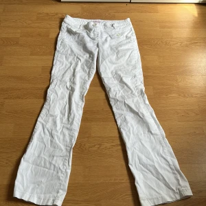 Vita bootcut byxor från Tally Weijl - Snygga vita bootcut byxor från Tally Weijl med knappar på fickorna fram och bak. Byxorna har låg midja och är gjorda i bomull, vilket gör dem sköna och lätta. Perfekta för dig som gillar en clean och fräsch look. 