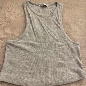 Ljusgrå ribbad linnetopp  - Superenkel och snygg ljusgrå ribbad linnetopp från Addax. Croppad modell med breda axelband och rund halsringning. Perfekt att matcha med jeans eller kjol för en chill look. Mjuk och stretchig i bomullsmix.