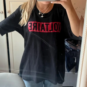 Svart Voltaire t-shirt med röd logga  - Cool svart t-shirt från Zadig & Voltaire med stor röd VOLTAIRE-logga på bröstet. Oversized passform och klassisk rund halsringning. Perfekt statement-plagg för dig som gillar streetstyle och enkel design.