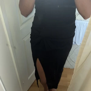 Svart långkjol med knyt och slits - Säljer en svart långkjol med snygg knytning i midjan och en hög slits framtill. Kjolen har en tight passform och är gjord i ett mjukt bomullstyg som känns skönt mot huden. Perfekt för dig som vill ha en stilren och trendig look.