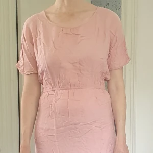 Rosa kortklänning med spetsdetaljer - Ljusrosa kortklänning med rund hals och korta ärmar. Klänningen har fina virkade spetsdetaljer i cirkelmönster längs axlar och nederkant. Resår i midjan.