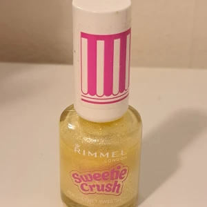 Rimmel Sweetie Crush nagellack gult - Nagellack från Rimmel London i serien Sweetie Crush, nyans 008 Sherbet Sweetheart. Färgen är glittrig gul med skimrande effekt. Söt design med vit kork och rosa detaljer. Perfekt för dig som vill ha en färgglad och lekfull look.