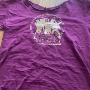 Lila Nasty Onkxx t-shirt med tryck - Cool lila t-shirt med korta ärmar och ett retroinspirerat tryck framtill med siluetter och texten 'Nasty Onkxx'. T-shirten har en avslappnad passform och är gjord i mjuk bomull, perfekt för en chill och personlig stil.