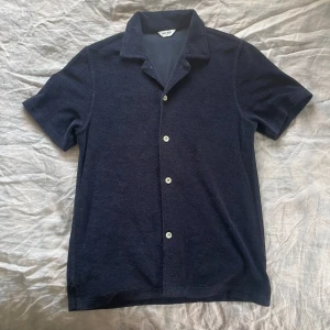 Mörkblå frottéskjorta från East West - Snygg mörkblå skjorta från East West i mjuk frotté. Skjortan har korta ärmar, klassisk krage och vita knappar framtill. Stl. XS. Perfekt skick och knappt använd! Nypris 600kr.