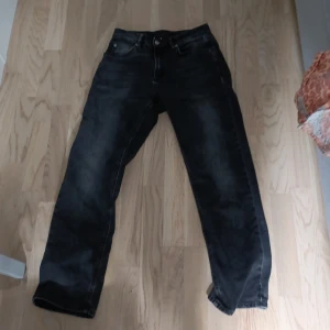 Svarta jeans från Nudie Jeans, 28/30 - Säljer ett par svarta jeans från Nudie Jeans i storlek 28/30. Jeansen har klassisk femficksdesign, raka ben och diskreta slitningar för en cool look. Materialet är jeans och färgen är mörksvart med lite tvättad känsla.