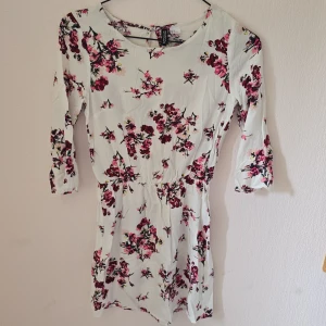 Blommig kortklänning från H&M Divided - Supersöt vit kortklänning med rosa och vinröda blommor från H&M Divided. Klänningen har trekvartsärm, markerad midja och knappdetalj i nacken. Perfekt för vår och sommar när du vill känna dig extra fräsch och feminin.