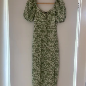Grön blommig långklänning Gina Tricot - Supersöt långklänning från Gina Tricot i grönt med vitt blommönster. Klänningen har puffiga korta ärmar, v-ringning med snörning framtill och en smickrande passform. Använd en gång men annars helt oanvänd. 
