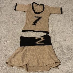 Beige stickad kortkjol med svart midja - Säljer en beige stickad kortkjol och topp set med svart bred midja och stor siffra framtill. Kjolen har en lätt utställd form och är perfekt för dig som gillar sportig och unik stil. Materialet är mjukt och stretchigt, vilket gör den bekväm att bära.