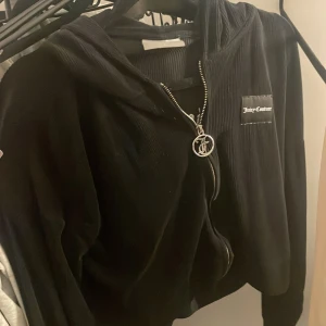 Svart Juicy Couture teddyjacka S - Svart kofta från Juicy Couture i storlek S. Jackan har dragkedja med snygg JC-logga, huva och broderad Juicy Couture-text på ryggen. Mjuk och skön med lång ärm, perfekt för en chill och trendig look.