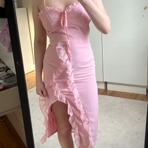 Rosa volangklänning med slits. Från shein! - Supersöt rosa klänning med smala axelband, volangdetaljer längs slitsen och knyt framtill. Från shein och använd 1 gång på ett bröllop. Strl xs. För liten på mig på bilden jag har strl S. 🥰säljer billigt. 