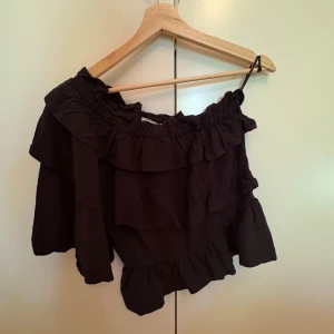 Svart volangblus från Copenhagen Muse - Supersnygg svart blus från Copenhagen Muse i storlek XS. Offshoulder-modell med volanger och en ärm, vilket ger en unik och trendig look. Nypris 1200kr. Använd endast fåtal gånger 