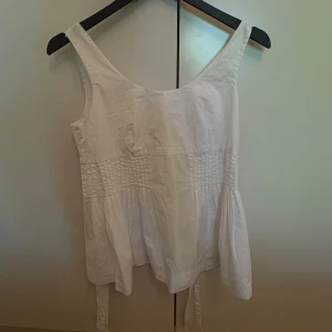 Vit linnetopp från COS med knyt - Supersöt vit linnetopp från COS i storlek 34. Toppen har breda axelband, smockad midja och knytband i sidorna. 