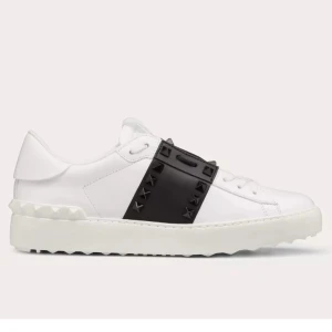 Valentino Open sneakers med nitar - Snygga vita Valentino Open sneakers med svart band och ikoniska pyramidformade nitar. Skorna har en chunky vit sula och är tillverkade i skinn. Perfekta för dig som gillar en stilren men edgy look. Köpta för 8,515 och köptes 2024 augusti, har kvar kartongen och alla grejer som den kom i! Självklart gör jag rent skira innan skick