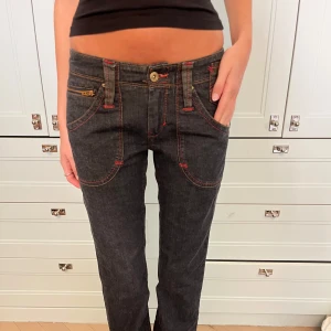 Levis jeans med röd kontrastsöm - Mörkblå jeans med raka ben, låg midja och snygga röda kontrastsömmar. Fickor med coola detaljer och bälte bak. 