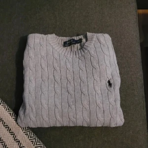 Ljusgrå stickad tröja från Ralph Lauren - Säljer en ljusgrå stickad tröja från Ralph Lauren. Tröjan har lång ärm och den ikoniska broderade loggan på bröstet. Perfekt för lager-på-lager under kyliga dagar. Det är en M men passar även S