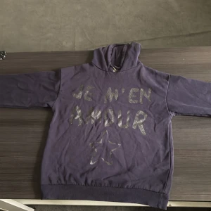 En mörk blå hoodie med text ”Je M’en amour - Denna tröjan är i ett bra skick det är inga fläckar eller hål! Det finns ett snöre som sitter vid halsen som är lite sönder men man tänker inte på det! 