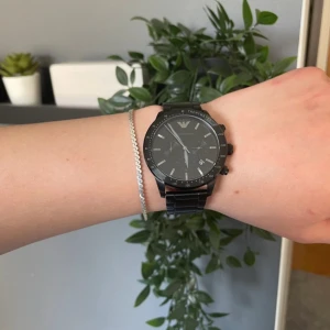 Svart Emporio Armani herrklocka - Stilren svart klocka från Emporio Armani med robust länkarmband i rostfritt stål. Klockan har kronograf, datumvisning och tydliga indexmarkeringar. Klassisk rund urtavla med diskret logga upptill. Perfekt accessoar för dig som gillar en clean och modern look. Nypris 3700kr