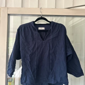 Mörkblå blus i linne från Uniqlo - Snygg mörkblå blus från Uniqlo i luftig linnemix. Blusen har v-ringning med snörning och trekvartsärmar med lätt puff. Storlek S. (Bra skick, näst intill oanvänd)