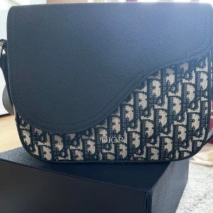  Oblique jacquard väska - Snygg axelväska med klassiskt monogrammönster i blått och beige canvas. Väskan har lock i svart skinn, justerbar axelrem och silverfärgade detaljer. Perfekt för dig som vill ha en lyxig och stilren accessoar med ikonisk logga.