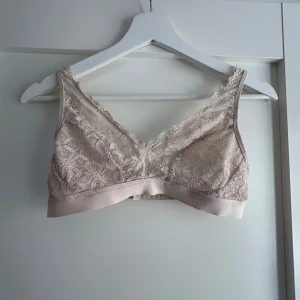 Beige spets bralette från Intimissimi - Supersöt beige bralette från Intimissimi med v-ringning och bred spetskant. Justerbara axelband och hakknäppning bak. Toppens spets har ett detaljerat mönster och mjuk känsla, perfekt för en chill och snygg look. Passar XS