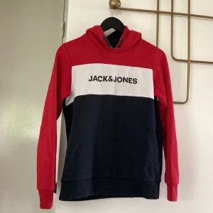 Jack & Jones hoodie i rött, vitt och blått - Snygg hoodie från Jack & Jones med färgblock i rött, vitt och mörkblått. Stor logga framtill, huva med snörning och långa ärmar. Perfekt för en chill och sportig stil. Mjuk bomullskänsla och relaxed fit.