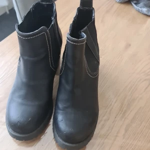 Svarta chelsea boots med klack - Snygga svarta chelsea boots i skinnimitation med markerade vita sömmar och elastiska partier på sidorna. Grov sula och stabil klack ger en cool look och extra höjd. Perfekta till jeans eller kjol för en trendig stil.