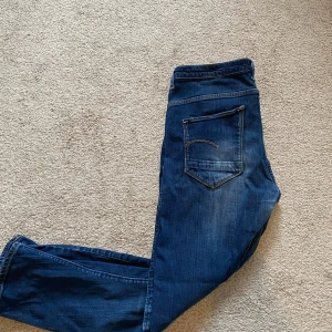 Mörkblå jeans från G-Star RAW - Säljer ett par mörkblå jeans från G-Star RAW med klassisk femficksdesign och snygga detaljer på bakfickan. Jeansen har normal passform och raka ben, perfekta till vardags. Stängs med dragkedja och knapp. Tveka inte på att höra av dig vid frågor eller funderingar! Mvh Sixten 