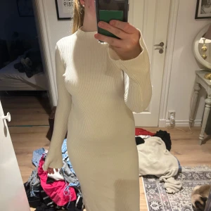 Ljusribbad långklänning från Gina Tricot - Säljer en ljus, ribbad långklänning från Gina Tricot. Klänningen har lång ärm, hög hals och figurnära passform. Perfekt för dig som gillar stilrena och enkla plagg med en modern touch.
