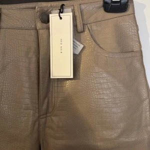 Taupe croc-mönstrade byxor från Neo Noir - Snygga taupe-färgade byxor från Neo Noir med croc-mönster. Byxorna har hög midja och raka ben. 